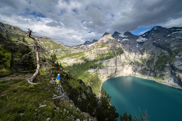 Hiker admiring Oeschinensee lake from steep mountain ridge, Bernese Oberland, Kandersteg, Canton of Bern, Switzerland
