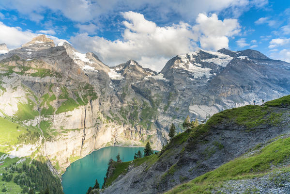 Hikers looking at Oeschinensee lake from a steep mountain ridge, Bernese Oberland, Kandersteg, Canton of Bern, Switzerland