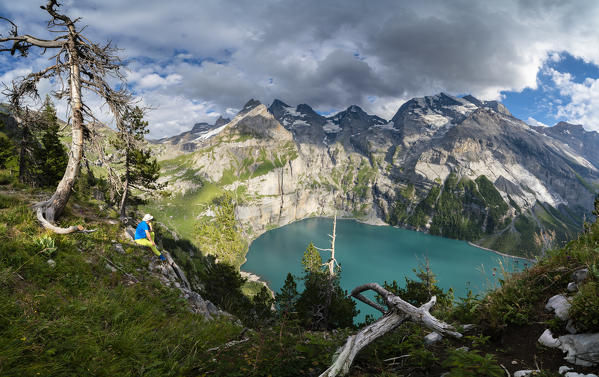 Panoramic of hiker on mountain ridge looking at Oeschinensee lake, Bernese Oberland, Kandersteg, Canton of Bern, Switzerland