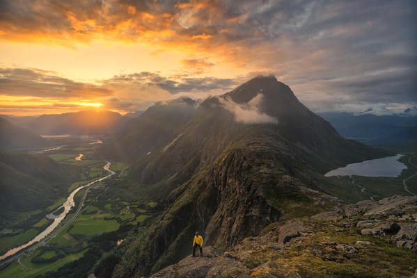 Hiker walking on Romsdalseggen ridge over Rauma valley lit by sun rays at sunset, Andalsnes, More og Romsdal county, Norway