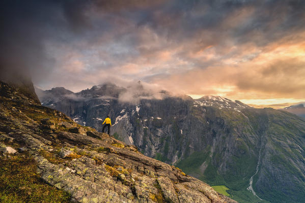 Rear view of man standing on Romsdalseggen Ridge admiring  Troll Wall mountain at sunset, Andalsnes, More og Romsdal, Norway