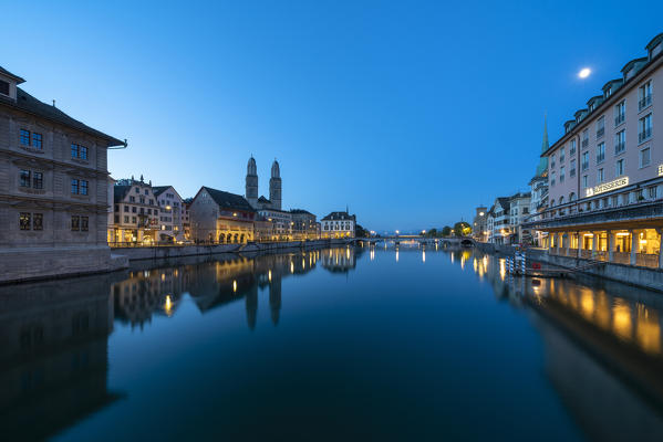 Illuminated buildings of Limmatquai and Grossmunster mirrored in Limmat River at dusk, Zurich, Switzerland