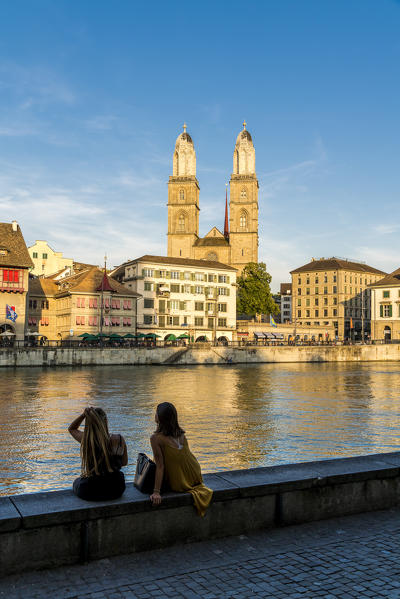 Rear view of young women admiring Limmatquai and Grossmunster Cathedral from banks of Limmat River, Zurich, Switzerland