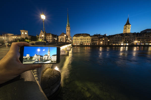 Fraumunster church at dusk mirrored in a smartphone screen on Munsterbrucke bridge, Zurich, Switzerland