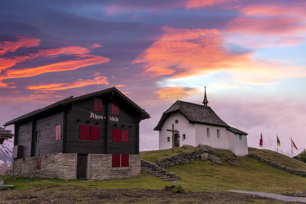 Pink sky at sunset over traditional chalet and chapel, Bettmeralp, canton of Valais, Switzerland