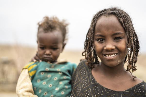 Portrait of smiling girl holding a baby boy, Melabday, Asso Bhole, Danakil Depression, Afar Region, Ethiopia, Africa