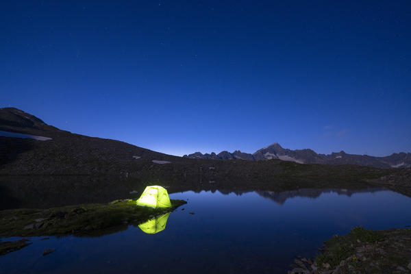 Illuminated tent of hiker on shores of  Obere Schwarziseeli lake at night, Furka Pass, Canton Uri, Switzerland