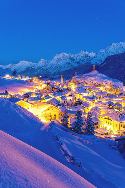 Snow covered village of Ardez brightly lit during the winter dusk, canton of Graubunden, Engadine, Switzerland