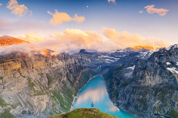 Hiker man with backpack admiring sunset over lake Limmernsee from top of rocks, aerial view, Canton of Glarus, Switzerland (MR)
