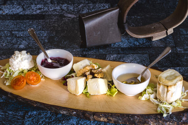 Goat cheese served with jam, honey and walnuts on wood chopping board, Italy