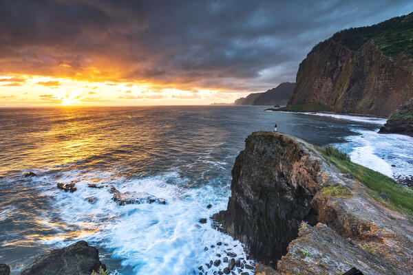 Man on cliffs looking at waves at dawn, Miradouro Do Guindaste viewpoint, Madeira island, Portugal (MR)