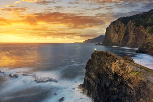 Hiker with head torch admiring sunrise from cliffs at Miradouro Do Guindaste viewpoint, Madeira island, Portugal