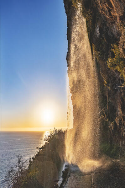 Spray of powerful Anjos waterfall on coastal road at sunset, Ponta do Sol, Madeira island, Portugal