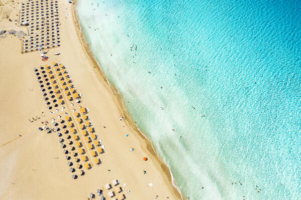 Beach umbrellas and sunbeds on white sand of Falassarna beach overlooking the crystal sea, aerial view, Crete island, Greece