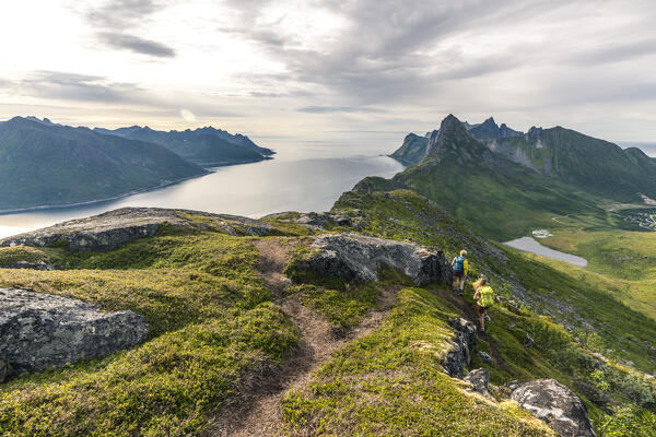 Young hikers with backpack walking on path on Barden peak to Segla mountain along the fjord, Senja, Troms county, Norway