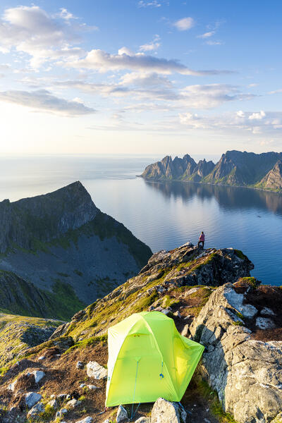 Hiker watching sunset out of camping tent on Husfjellet mountain peak, Senja island, Troms county, Norway