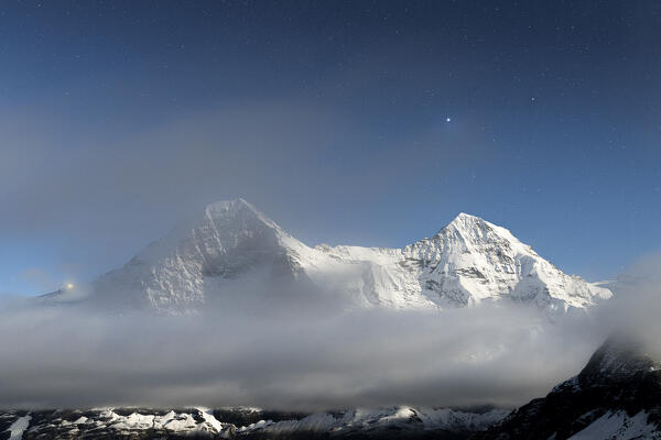 Starry sky over the snowcapped Eiger and Monch mountains covered by fog at night, Mannlichen, Bern canton, Switzerland