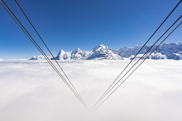 Cableway hidden by fog with Eiger, Monch and Jungfrau peaks covered with snow on background, Murren Birg, Bern, Switzerland