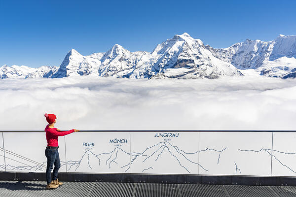 Woman admiring Eiger, Monch and Jungfrau mountains in the mist from panoramic walkway, Murren Birg, Bern, Switzerland