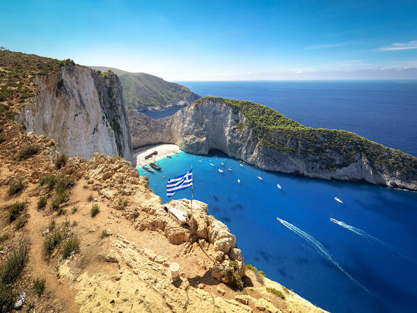 Greek flag on top of majestic cliffs, viewpoint of the famous Shipwreck Navagio Beach, Zakynthos, Greece