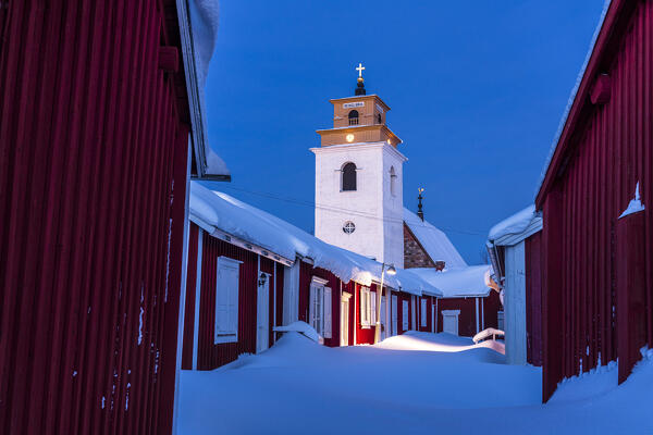 Winter dusk over the old bell tower and wood cottages covered with snow, Gammelstad Church Town, Lulea, Sweden