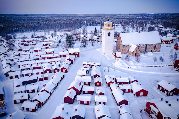 Aerial view of red cabins and church covered with snow at dusk with Lapland forest on background, Gammelstad, Lulea, Sweden