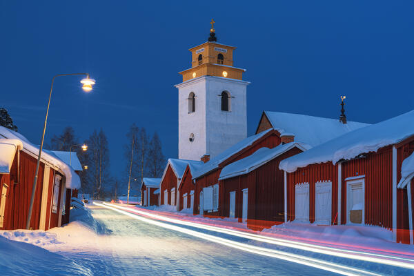 Lights trails of cars on the icy road crossing the medieval Gammelstad Church Town covered with snow at night, Lulea, Sweden