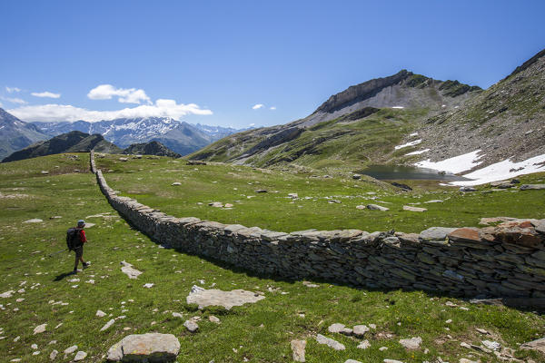 Hiker looking at the wall built for the livestock that divides Pian dei Cavalli. Pian dei Cavalli, Campodolcino, Vallespluga, Valchiavenna, Lombardy, Italy.
