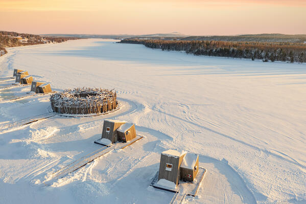 Aerial view of the floating Arctic Bath Hotel and its wood cabins in the snow at sunset, Harads, Lapland, Sweden