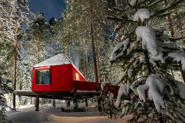 Red hut in the winter forest covered with snow at dusk, accommodation for tourists of the Tree hotel, Harads, Lapland, Sweden