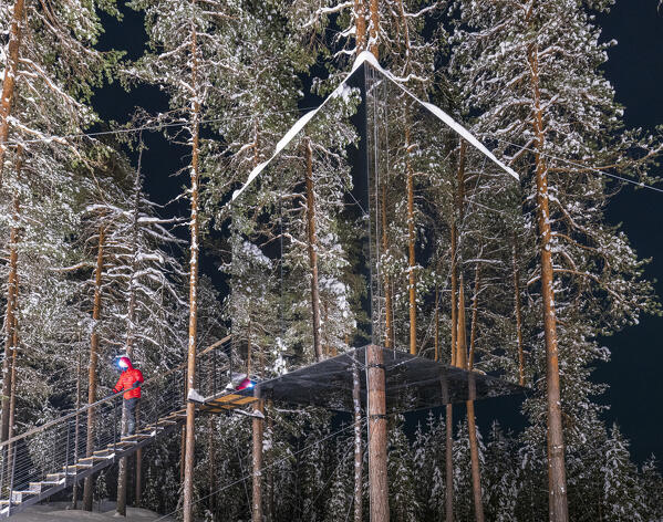 Hiker walking on steps leading to the cube shaped cottage with mirrors on the snowy trees, Tree hotel, Harads, Lapland, Sweden