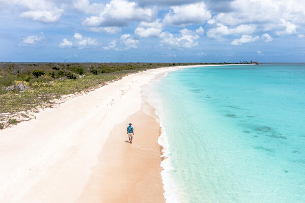 Aerial view of carefree man with straw hat walking on idyllic beach washed by the turquoise sea, Antigua & Barbuda, Caribbean
