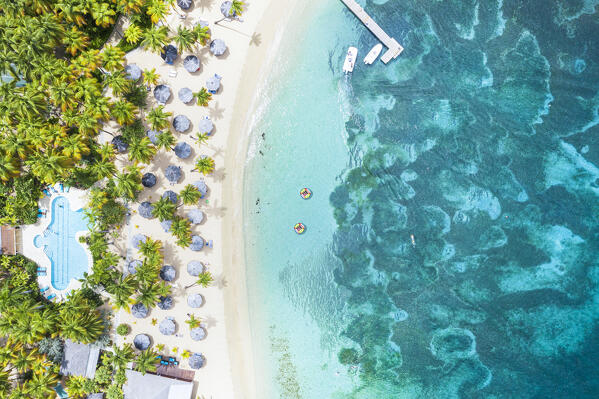 Luxury resort with swimming pool and beach umbrellas on palm fringed beach from above, Antigua, Caribbean, West Indies