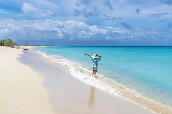 Rear view of cheerful woman holding the straw hat while playing with waves, Barbuda, Antigua & Barbuda, Caribbean, West Indies