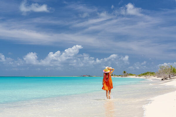 Woman with sun hat walking on a white sand beach washed by waves, Barbuda, Antigua & Barbuda, Caribbean, West Indies