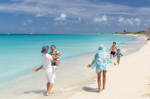 Cute little brothers and sister running and jumping into father's arms on a beach, Antigua and Barbuda, Caribbean, West Indies