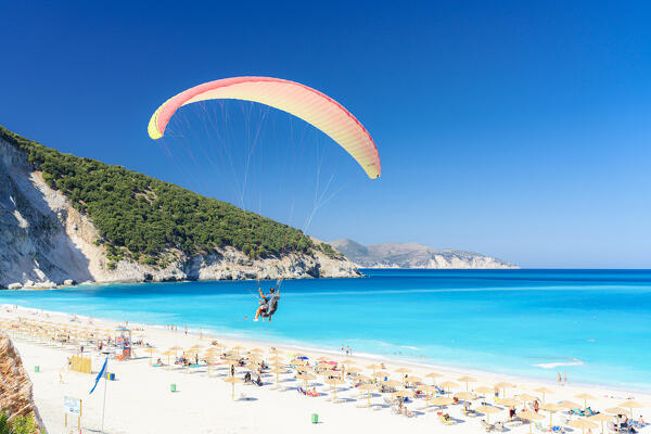 Tourists paragliding over the equipped Myrtos beach washed by crystalline water of Ionian Sea, Kefalonia, Greece