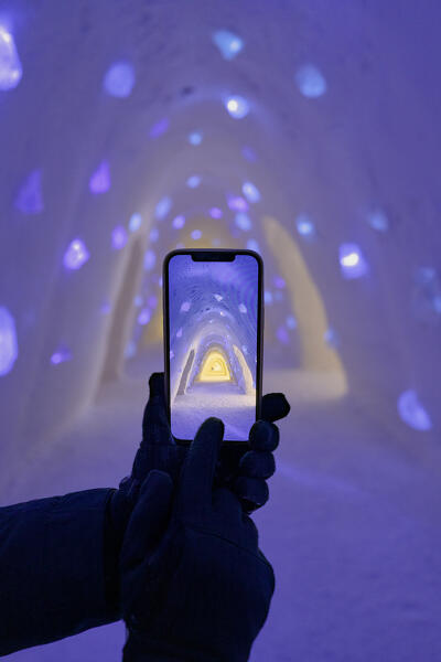 Personal perspective of tourist photographing the ice tunnel with smartphone inside Lainio Snow Village, Kittila, Lapland, Finland