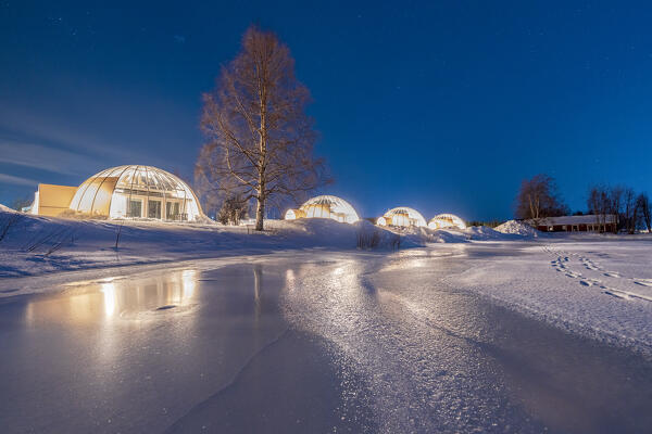 Starry sky at dusk over the illuminated glass igloo on the snowy shores of the frozen river Kalix, Norrbotten county, Lapland, Sweden