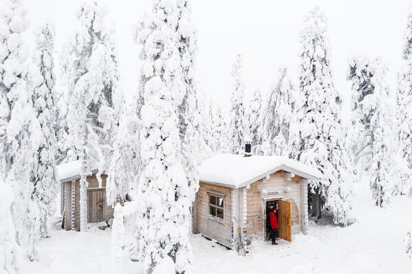 High angle view of woman admiring the snowy forest from a lone mountain hut, Iso Syote, Northern Ostrobothnia, Lapland, Finland