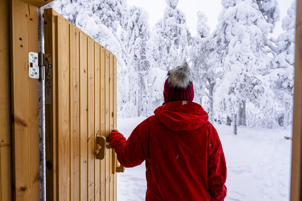 Woman admiring the snowy forest standing at the entrance of a mountain hut, Iso Syote, Northern Ostrobothnia, Lapland, Finland
