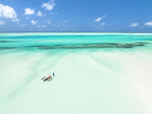 Lone fisherman with dhow approaching to the crystal sea from the shallow waters of lagoon, Paje, Jambiani, Zanzibar, Tanzania