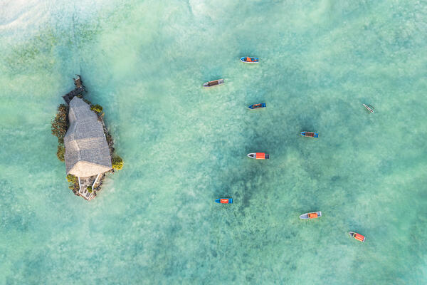 Overhead view of moored boats in the crystal sea nearby the iconic restaurant set on a rock, Pingwe, Michamvi, Zanzibar, Tanzania