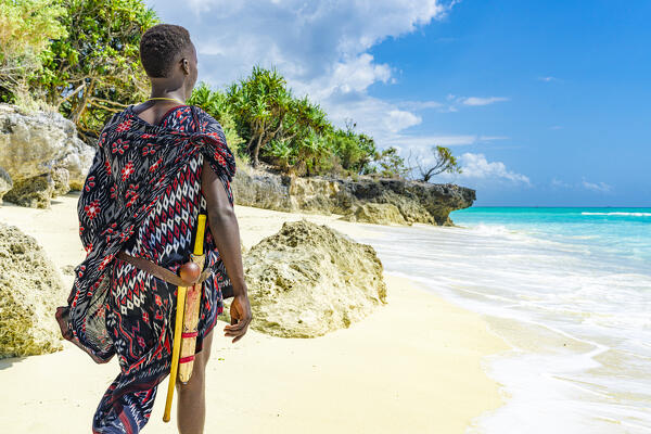 Young Maasai warrior walking on idyllic white sand beach, Zanzibar, Tanzania