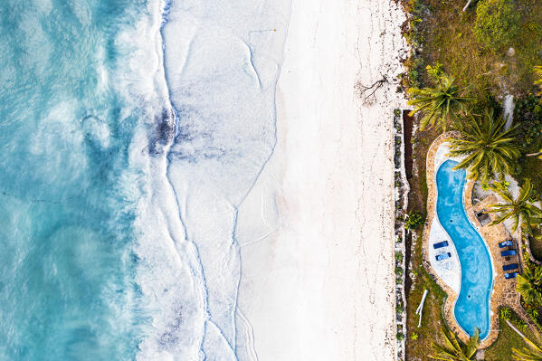 Swimming pool of a tourist resort on white coral beach washed by waves, overhead view, Zanzibar, Tanzania