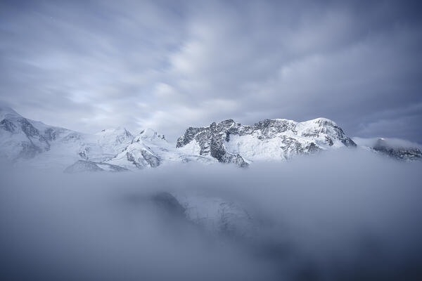 Clouds over the snowy Castor, Pollux, Roccia Nera, Breithorn in fog at dusk, Gornergrat, Zermatt, canton of Valais, Switzerland