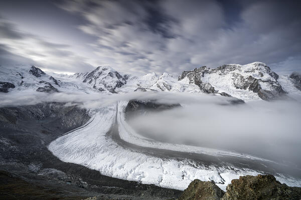 Mist over Monte Rosa glacier and snowy mountains under scenic clouds at dusk, Gornergrat, Zermatt, canton of Valais, Switzerland