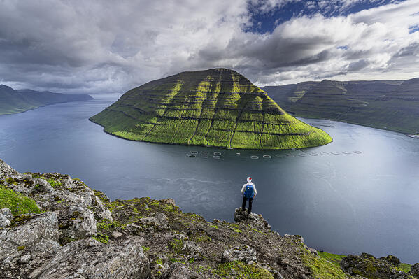 Hiker with backpack looking at Kunoy Island and ocean standing on Klakkur mountain, Klaksvik, Bordoy Island, Faroe Islands (MR)
