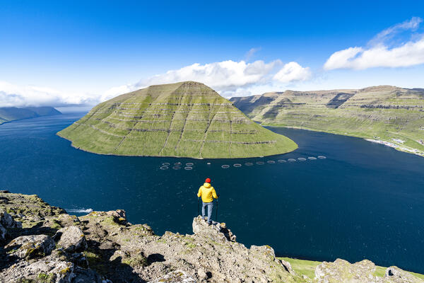 Hiker admiring the fjord and Kunoy Island standing on rocks on Klakkur mountain, Klaksvik, Bordoy Island, Faroe Islands