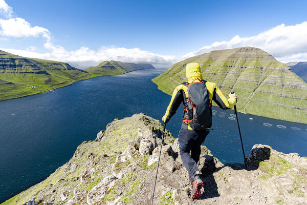 Hiker man with trekking poles conquering Klakkur mountain peak above the fjord, Klaksvik, Bordoy Island, Faroe Islands (MR)